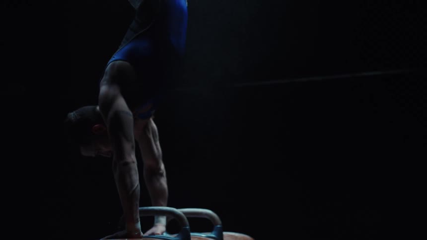 A male gymnasts performing acrobatic moves in a dark room