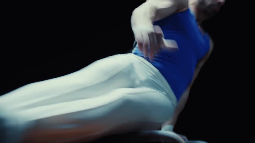 A male gymnast swings skillfully on a pommel horse during practice in a darkroom