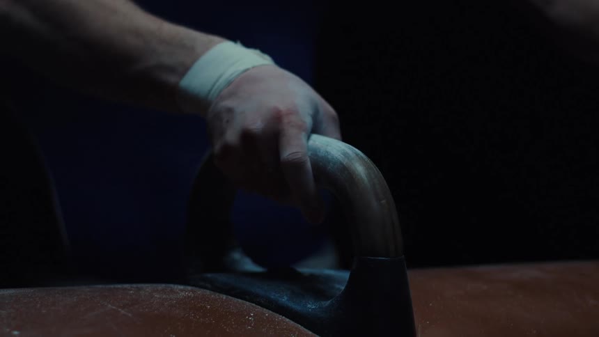 This video is a closeup shot of a gymnasts chalked hand gripping one of the handles or pommels on the pommel horsethe shot is tightly framed and darkly lit emphasizing the texture of the chalk on the hand and the surface of the apparatus
