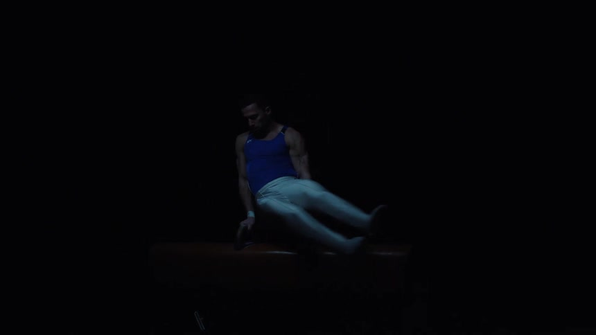 Gymnast performing a move on the pommel horse under minimal lighting