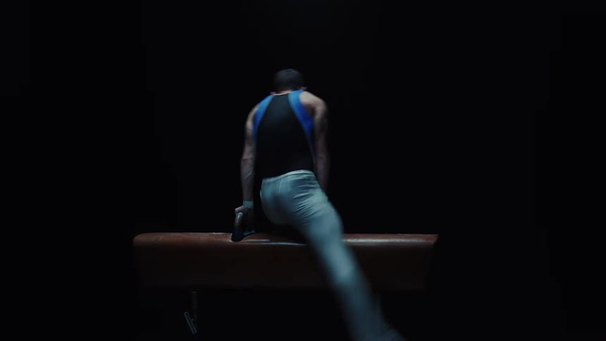 Under a dramatic spotlight a male gymnast demonstrates incredible strength and control as he executes a fluid and powerful routine on a pommel horse