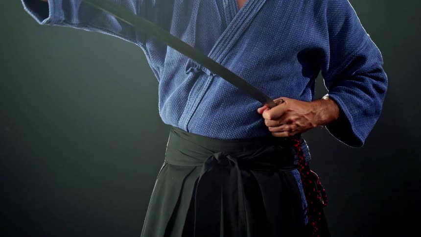 Close up of a male japanese martial artist sheathing their sword while standing in a dark room