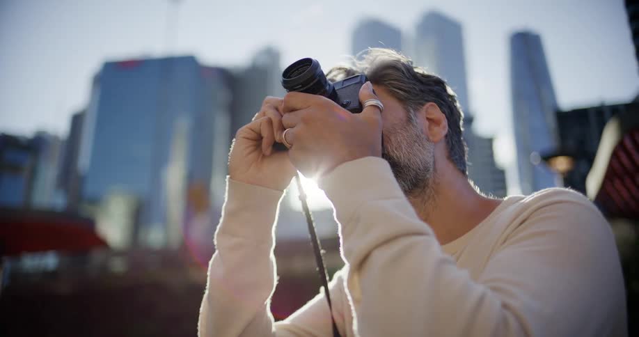 Man using a camera outdoors with buildings in the background