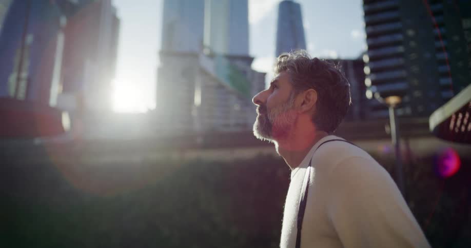 Close up of a middle aged man visually appreciating high rise buildings while walking outdoors in a metropolitan city at sunrise