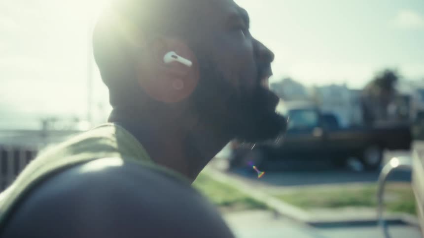 Man sitting on a bench outdoors holding a smartphone with wireless earbuds