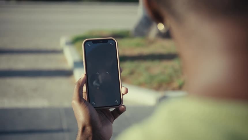 A man holding up a smartphone while sitting in a suburban outdoor area