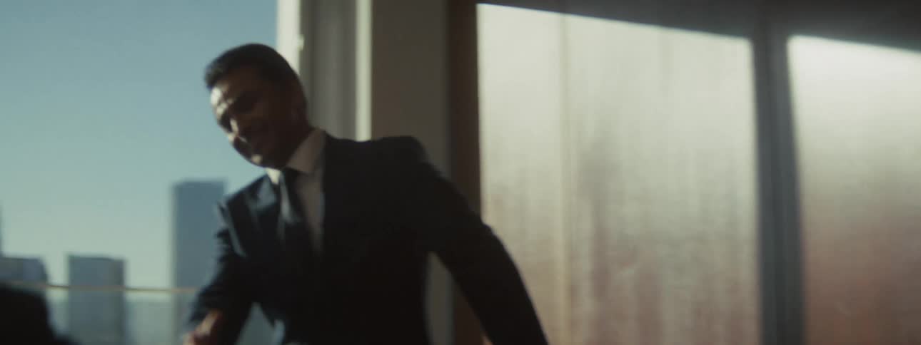 Young adult man wearing formal clothes arrives at a business meeting and shakes the hand of another man sitting and waiting for him indoors during day time