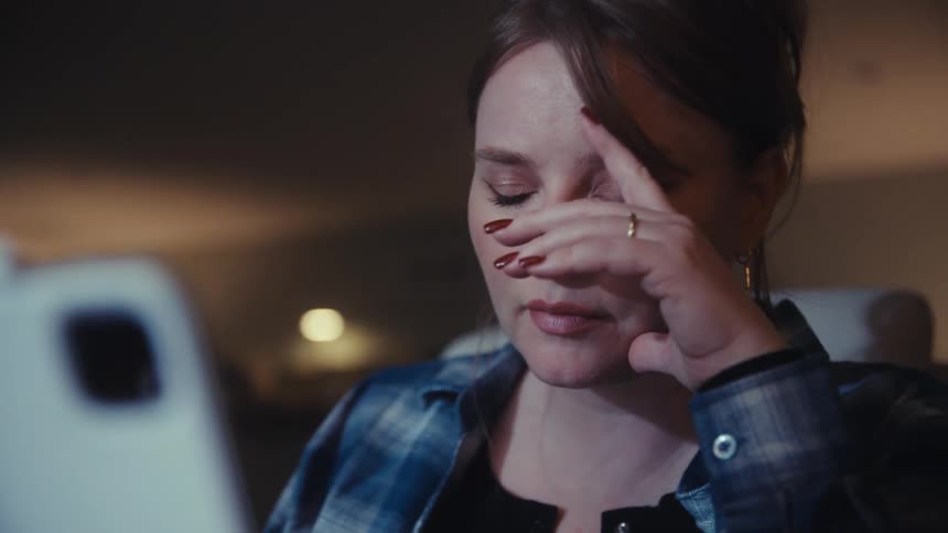Woman looking at a device while bringing her hand to her face indoors
