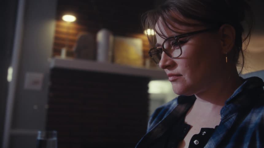 A woman wearing glasses works at a desk with multiple screens and smiles