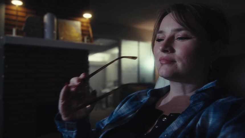 Woman removes her glasses while seated in an indoor environment