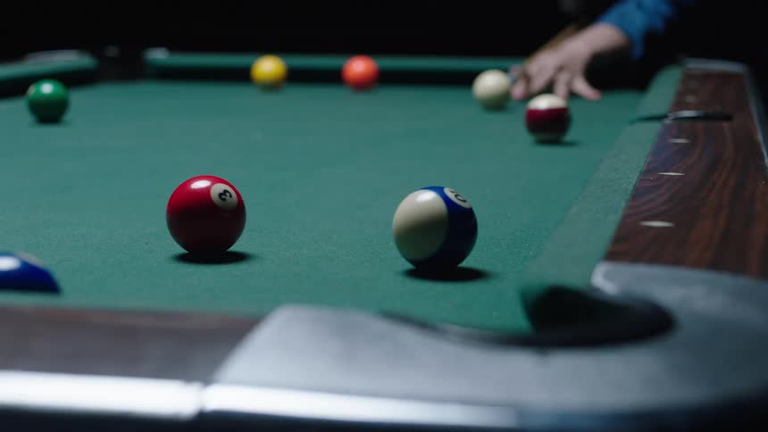 A persons hand is shown making a shot on a pool table with many pool balls