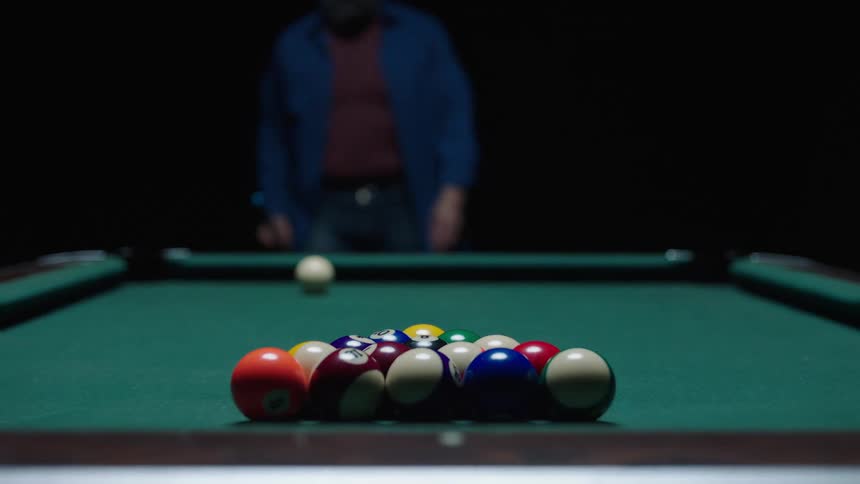 A bald male is positioning a pool stick in front of the white ball on a pool table to take a shot
