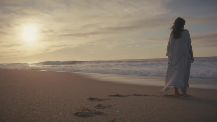 Woman walking on the sand near the sea during sunrise