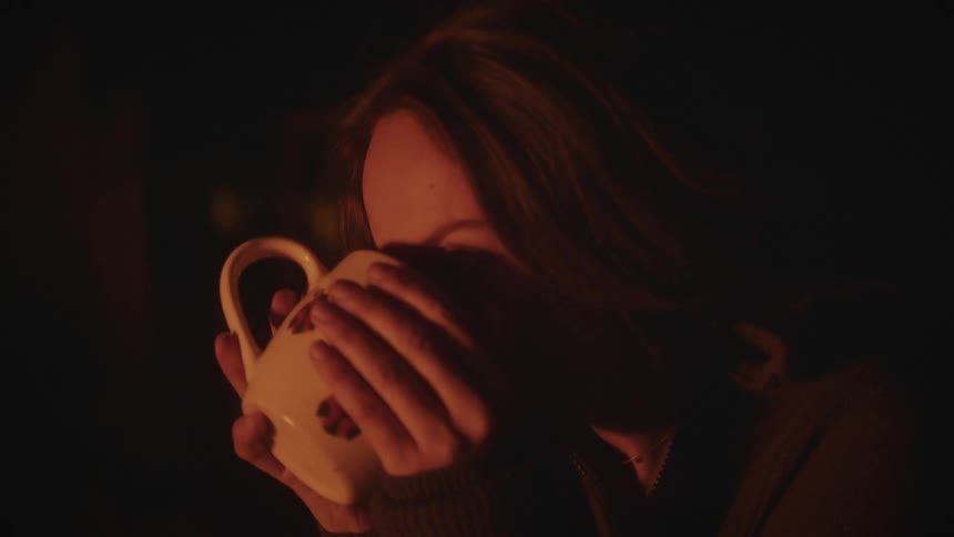 Woman drinks from a mug in a dimly lit room