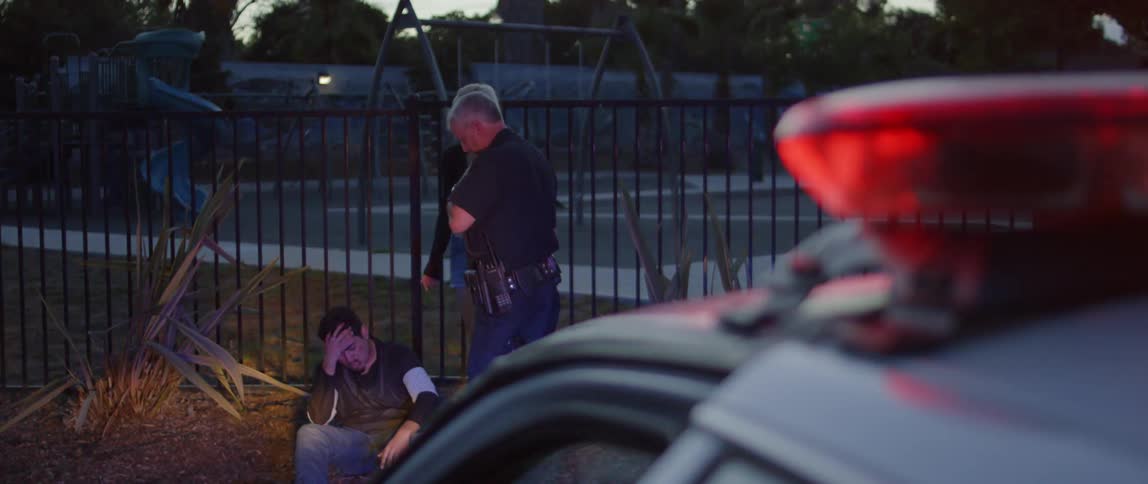 A man sits as a cop talks to him