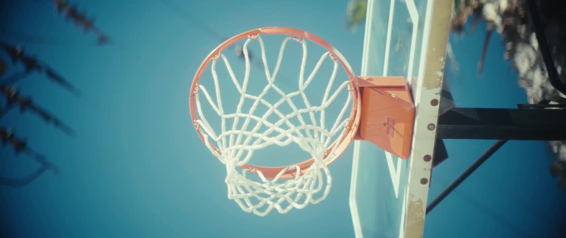 Sunlgiht shines on a basketball hoop and backboard as a basketball flies through the hoop