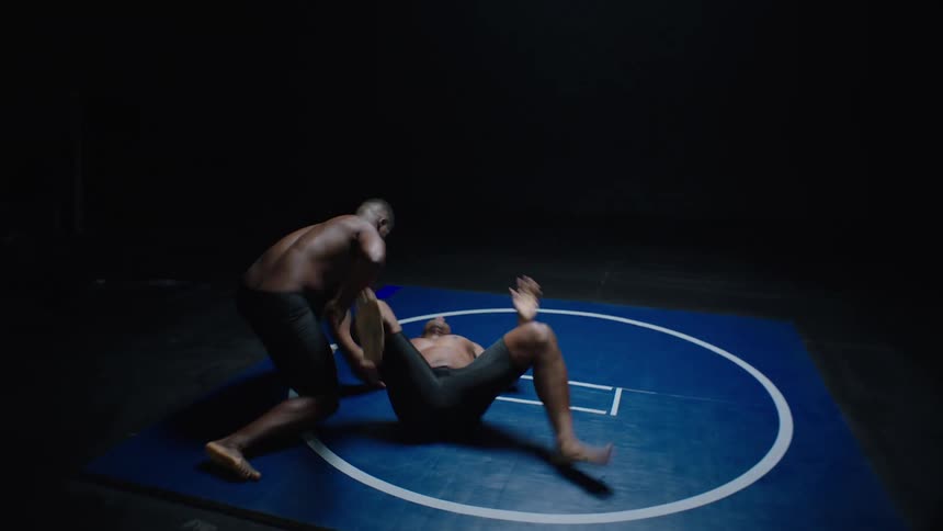 Two wrestlers in a ring as wrestler takes down the other man and lies on top of him