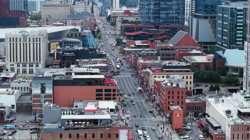 Vehicular and pedestrian traffic move along a wide street passing through downtown during the daytime