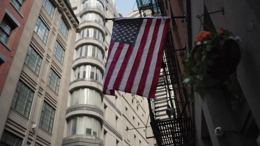 United states flag hanging from the facade of an urban building with metal fire escapes and tall buildings around