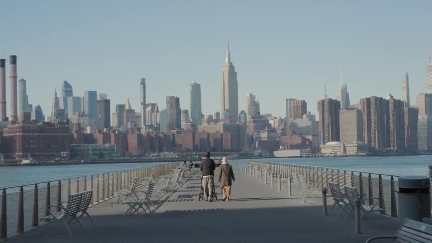 Parents with a stroller walk along a pier across from a skyline on a misty day
