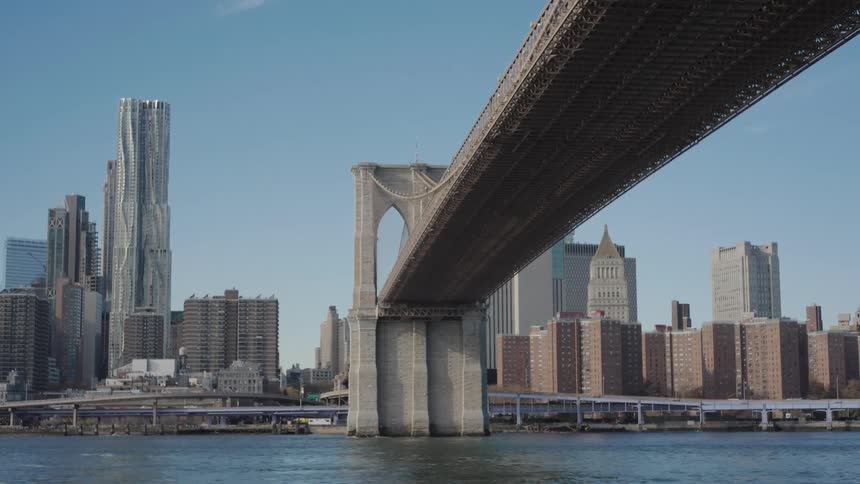 Traffic moves along the waterfront highway passing under a suspension bridge located near downtown during the daytime