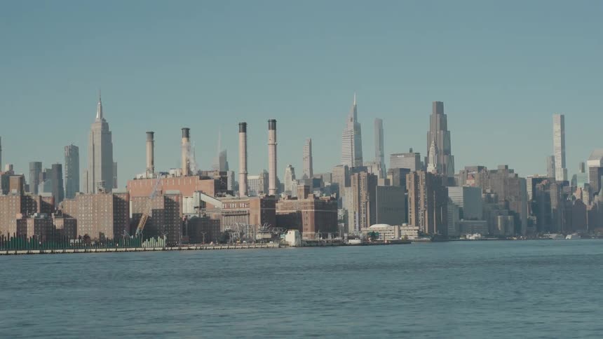 Metropolitan city along the coast with cranes on the loading dock as traffic moves on the street