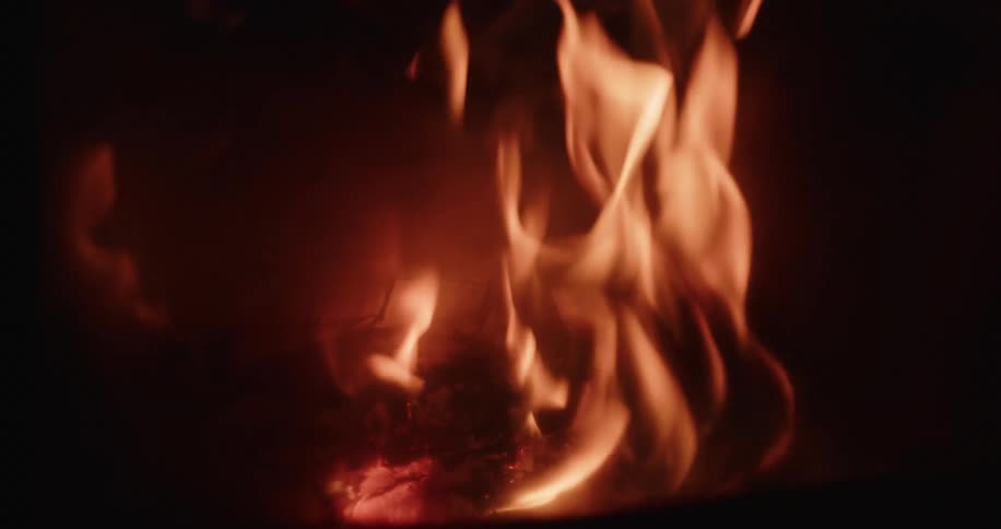Orange flames rise from burning wood inside a dark environment