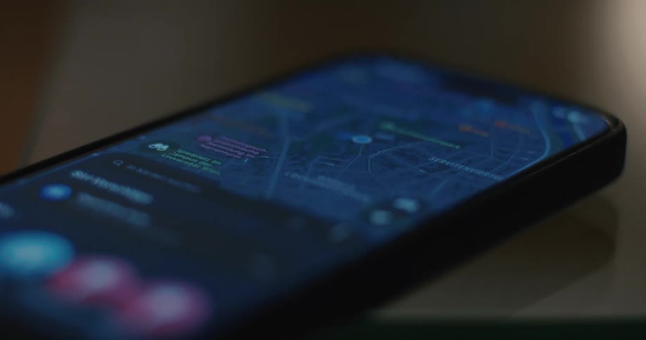 A smartphone lies on a dark table displaying a blue map application with street names and various location icons