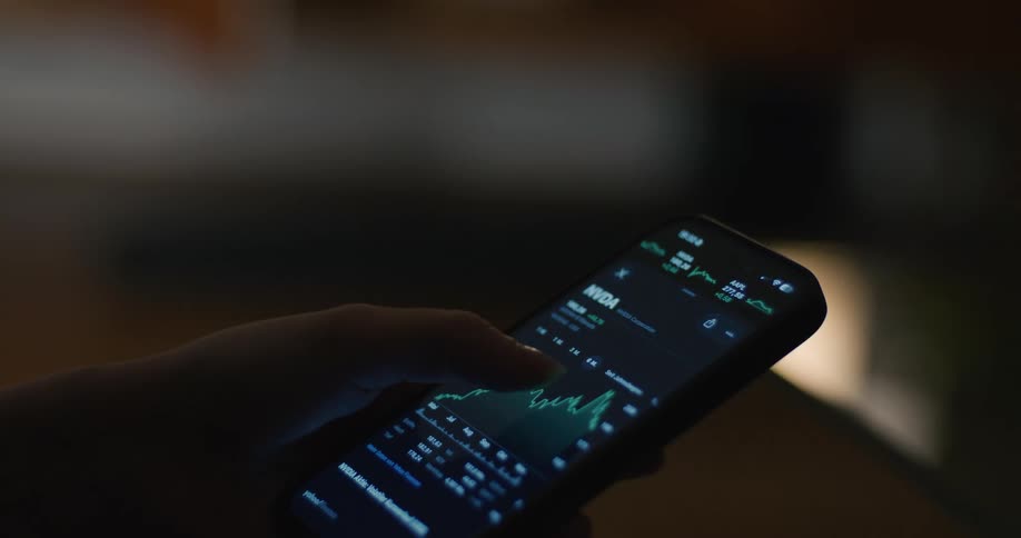 Hand holding a smartphone displaying a financial chart on a lit screen