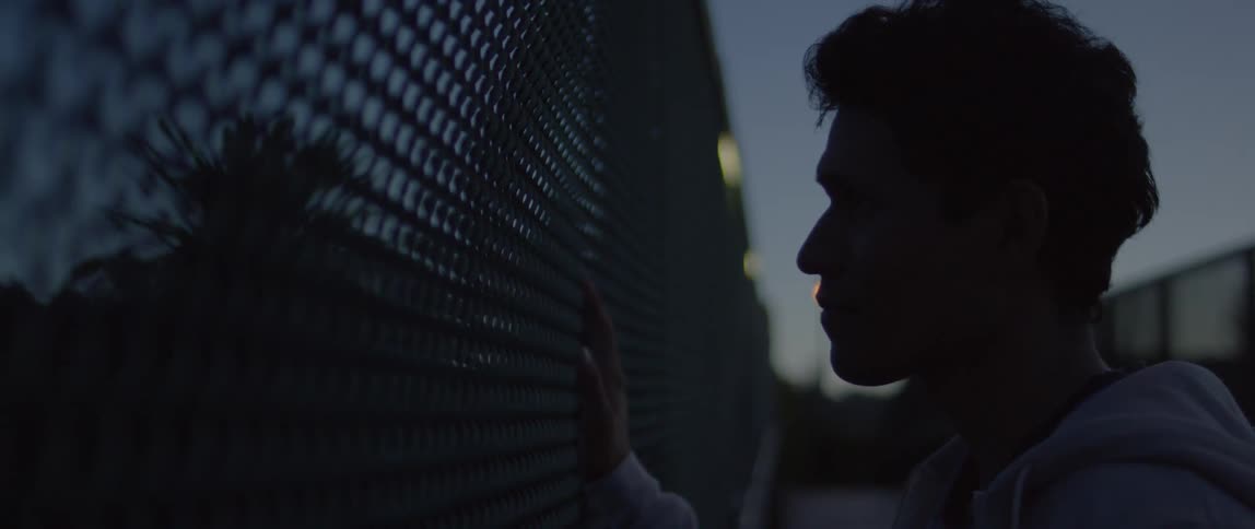 A man touches a chain link fence at night