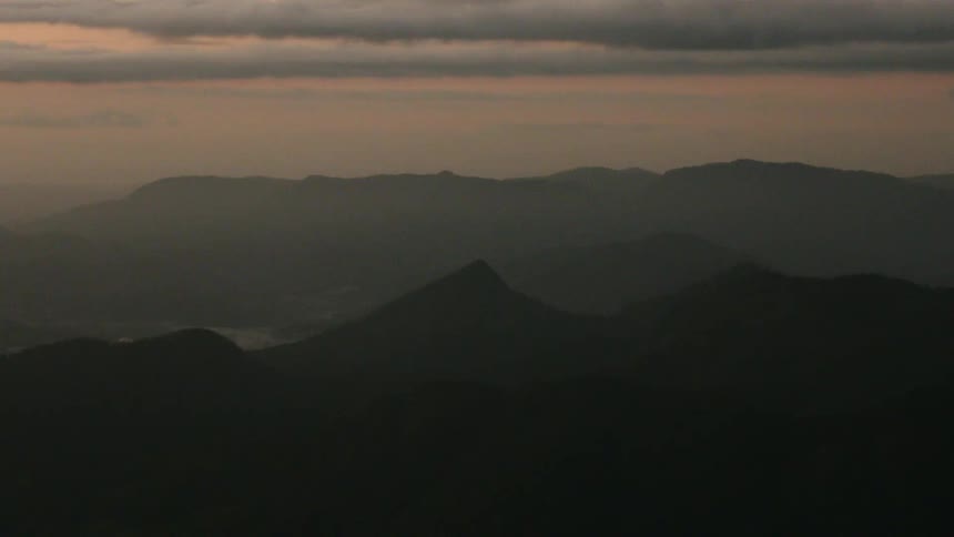 A wide shot of a multilayered mountain range and hills in silhouette seen at twilight under a cloudcovered sky the hills fade into the distance creating an atmospheric perspective