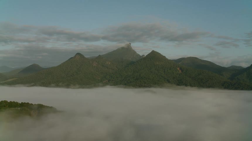 Thick blankets of white mist obscure the deep valley floor leaving only the rugged green mountain peaks to bask in the soft warm glow of early morning light under a vast cloudy sky