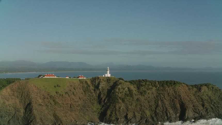 Lighthouse and buildings overlooking the coast as waves splash against the promontory