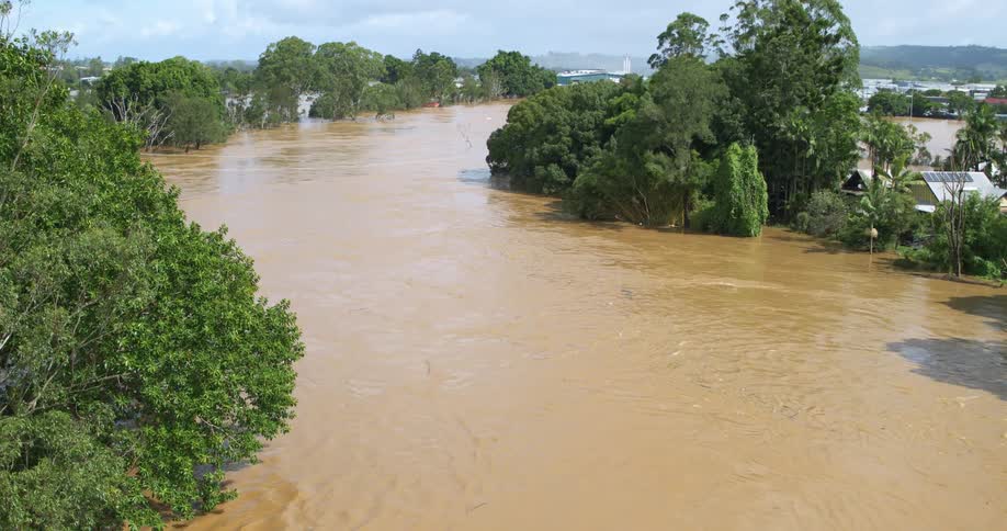 Aerial view of a muddy flood river flowing past suburban houses and trees