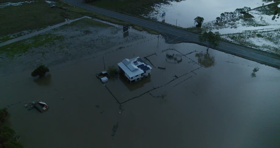 A building sits in the middle of a flooded area with a road nearby at midday
