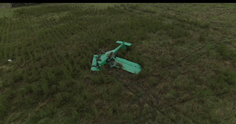 Aerial view of a crashed small aircraft lies abandoned in the middle of a grassy field
