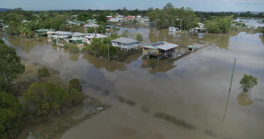 The video shows an aerial view of a residential area heavily impacted by floodwaters many houses are partially submerged with the muddy water covering roads and fields up to the floor levels of the elevated homes