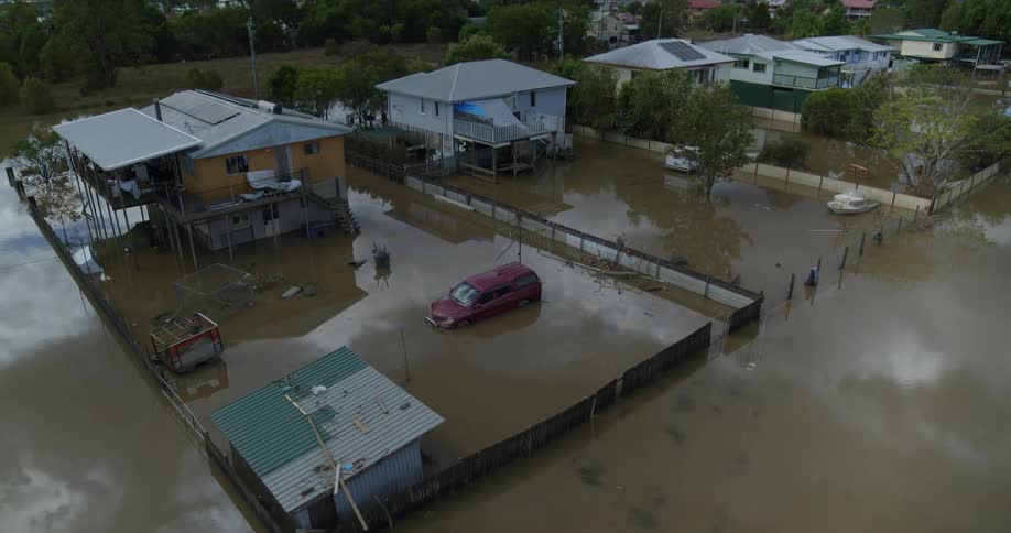 Aerial view of a flooded neighborhood with a van and small boat in yards filled with high water