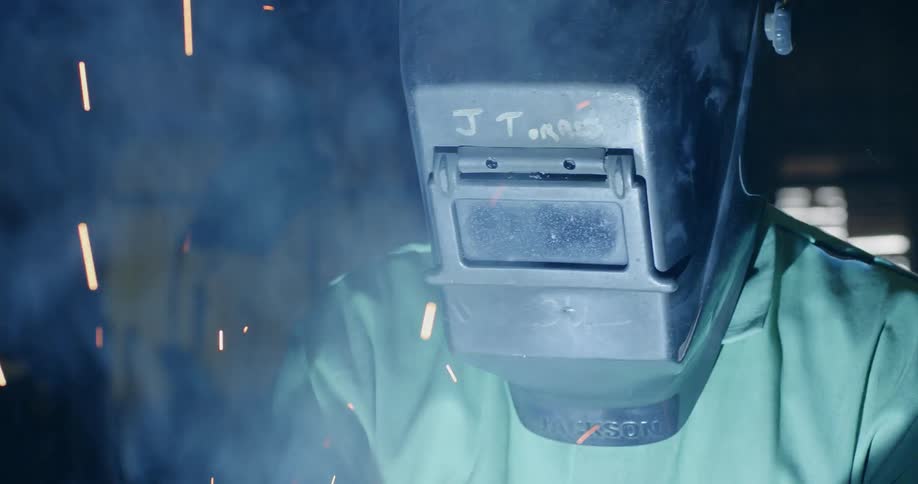 Sparks and smoke fly around a welder's mask