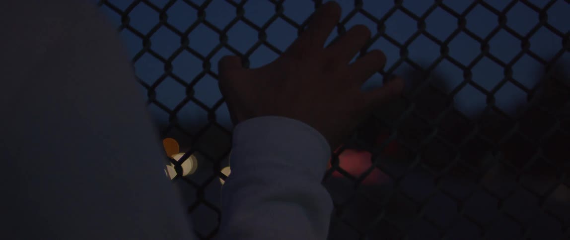 A person with their hand on a metal fence at night