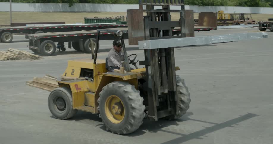 A forklift drives lifting up a large beam