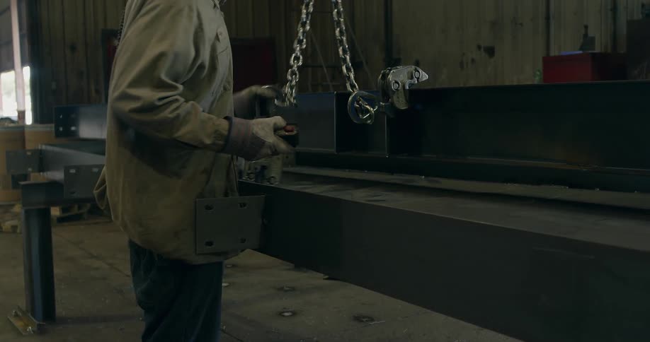 A man attaches a chain to a large metal beam in a factory