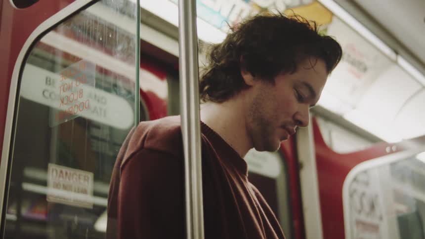 The face of a man inside a subway car looking at a piece of paper while giving a subtle smile