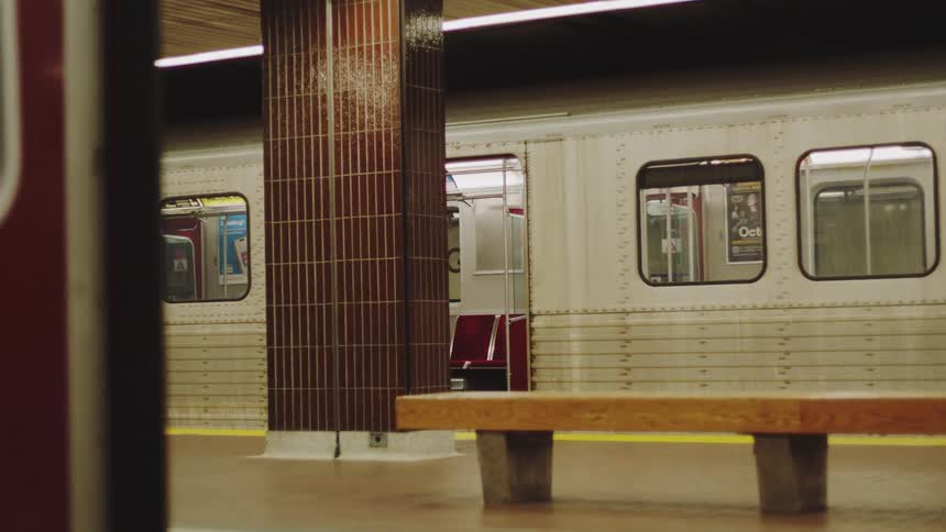 A red subway door slides shut in the foreground obscuring the view of the tiled station platform and a waiting train