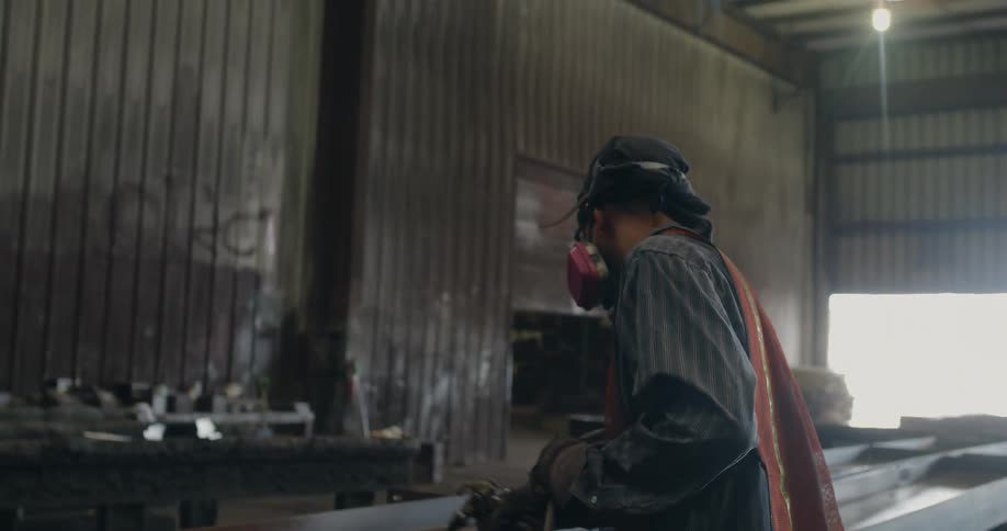 Man wearing an orange vest and mask sprays water on metal