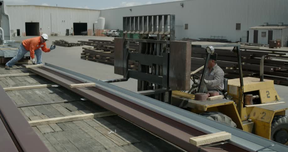 Men load beams onto a semi truck with a forklift