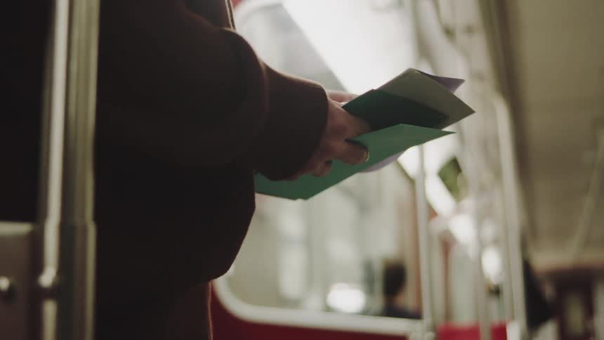 A man stands inside a subway car shuffling through a stack of papers in his hands