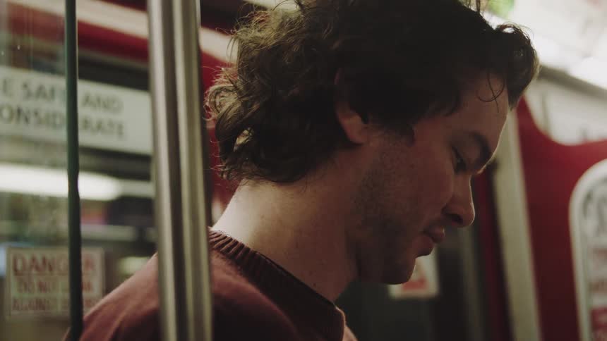 Young adult man talking and smiling while standing up on a subway indoors