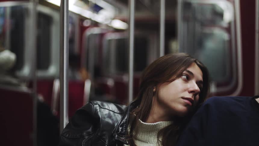 A woman leans on a mans shoulder as they sit together on a moving subway train