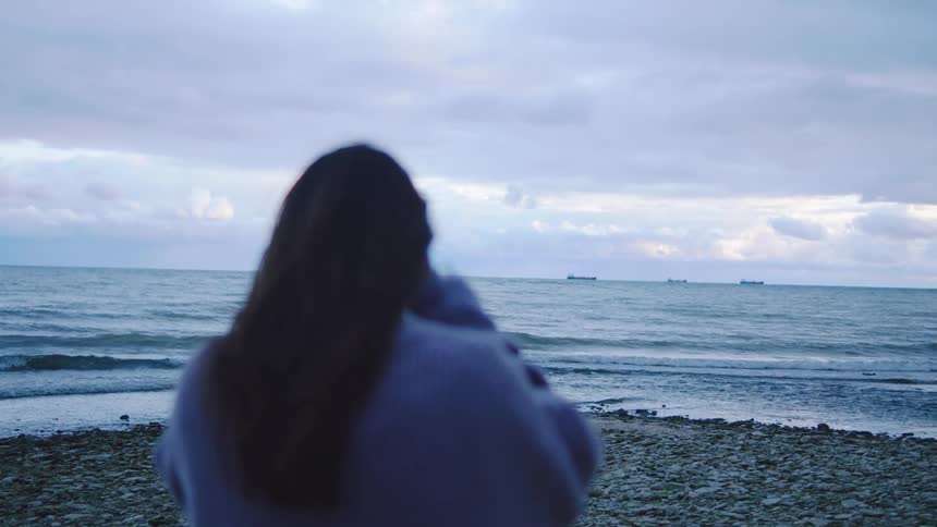 Woman smiles in the foreground facing the sea under a cloudy dusk sky